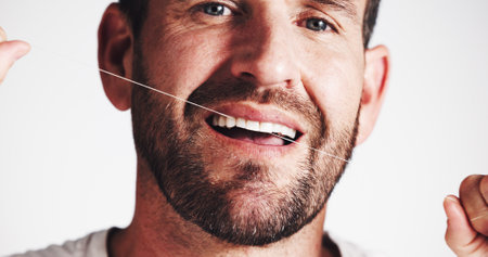 Dental health, studio and man floss teeth for oral hygiene, gum wellness or self care on white background. Cleaning tooth, string and portrait with morning routine, plaque removal and fresh breathの写真素材