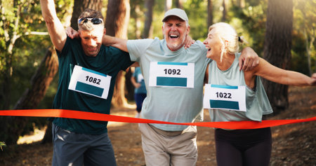 Win, people running and help to finish line for exercise aid, fitness or champion in forest. Mature team, excited runner and celebration for race with success, goal and sports achievement at marathonの写真素材