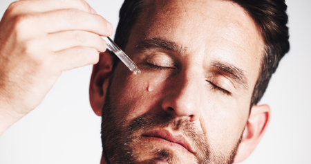 Serum, beauty and glow with man in studio for skincare treatment, anti aging benefits and hydration. Collagen, shine and oil dropper with mature person on white background for cosmetics and self careの写真素材