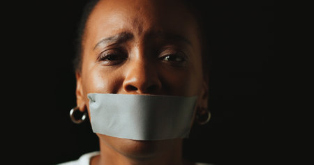 Woman, tape and mouth with stress in studio for silence, voice and anxiety by black background. African person, cover lips and portrait with depression, sad and mental health with space in Nigeriaの写真素材