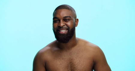 Black man, portrait and smile in studio for skincare, confidence and grooming in morning. African person, dermatology and happy on blue background space for beard care, topless and hygiene in Nigeriaの写真素材