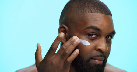 Portrait, cream and black man in studio, cosmetics and dermatology on blue background. African...