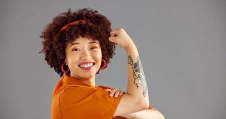 Portrait, flexing arms and woman with power, smile and win with confidence on grey studio...