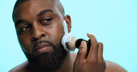 Brush, foam and shaving with black man in studio, cosmetic care and product with skincare on blue background. Space, cream or facial maintenance for hair removal, beauty or grooming for hygieneの写真素材
