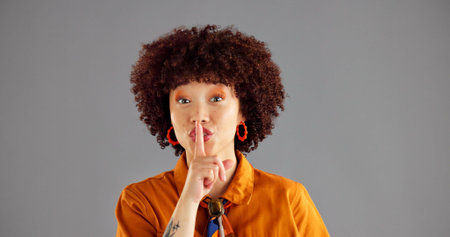 Silent, finger and portrait of woman in studio for gossip, secret and privacy on gray background. Mockup space, emoji and isolated person with gesture for shh, noise or whisper for confidential newsの写真素材