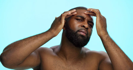 Studio, face check and skincare for man, portrait and acne treatment in morning, serious and dermatology. Blue background, self care and black person with routine for beauty, inspection and worryの写真素材