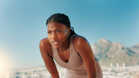 Tired, black woman and fitness with break in nature for workout, intense exercise or training. Active, female person or runner with recovery or rest for outdoor cardio, health or wellness on mountainの写真素材