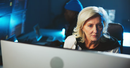 Woman, hacker or reading on computer at night for programming, cyber attack or online information. Mature person, pc or late research for website phishing, data protection or criminal with fraud riskの写真素材