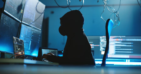 Night, hacking and person with hoodie, computer and programming of cyber attack, screen and system. Mysterious, criminal and typing of scam for ransomware, anonymous and hacker with tech for phishingの写真素材