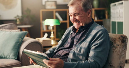 Senior man, tablet and laugh on couch, relax and happy with streaming, movie and comedy show on web in home. Elderly person, touchscreen and app for funny film, social network and smile in retirementの写真素材