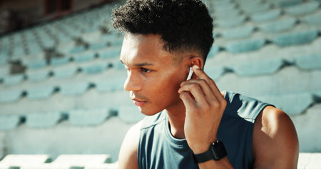 Man, athlete and earphones at stadium with music, break and listening with track for fitness in...