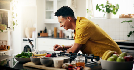 Cooking, laptop and smile with man in kitchen of home for hobby, meal prep or nutrition. Ingredients, online recipe and passion with happy person in apartment for diet, health or supper as chefの写真素材
