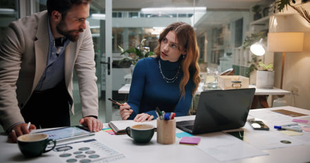 Business people, notebook and tablet in office for discussion, project feedback and advice at night. Journalist team, planning and tech in agency for article notes, collaboration and late informationの写真素材