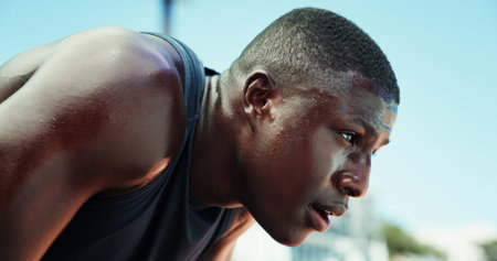 Runner, black man and tired with sweating at stadium for race competition, endurance challenge and breathing. Fitness, athlete and sports fatigue outdoor for running recovery, burnout or workout restの写真素材