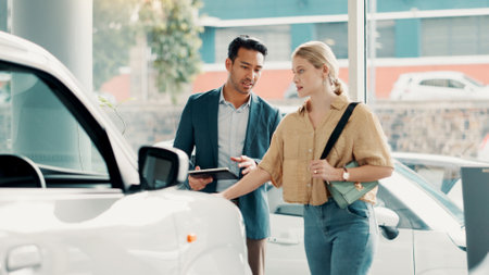 Tablet, customer and salesman with pitch for car dealership, transport model and motor for rental service. Showroom, woman and male seller with tech for assistance, vehicle features and communicationの写真素材