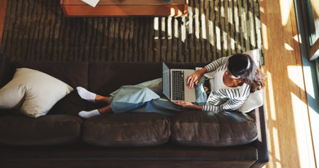 Computer, sofa and above of woman in home for research, browse website and internet, Relax, living room and top view of person on laptop for typing email, connection and communication in houseの写真素材