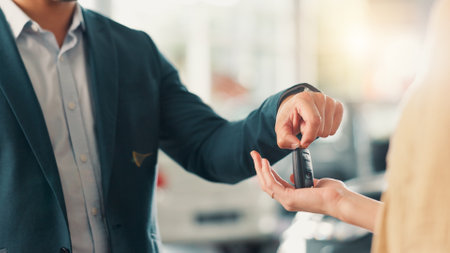 Showroom, salesman and customer with hands for car keys, test drive or success purchase of motor. Dealership, people or giving equipment in closeup for buying vehicle, rental service or auto by flareの写真素材