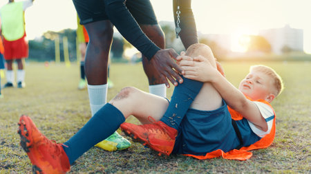 Soccer, child and player for injury, knee pain and muscle tension for scrape in sports competition. Football field, hands and coach with boy for helping, support and tendinitis emergency for kidの写真素材