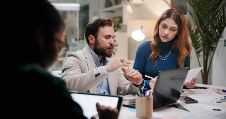 Business, teamwork or planning with laptop in office at night for marketing campaign, design feedback and strategy. Graphic designer, people and discussion for brand development, ideas and overtimeの写真素材