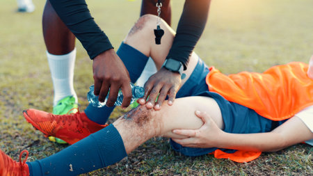 Soccer, child and water for injury, knee pain and muscle tension for scrape in sports competition. Football field, hands and coach with boy for helping, support and tendinitis emergency for kidの写真素材