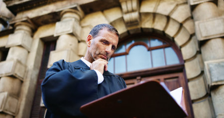 Thinking, reading and judge and mature man in city for trial report, policy legislation and legal documents. Lawyer idea, attorney paperwork and vision with person at courtroom outdoor in low angleの写真素材