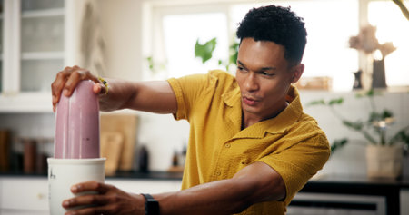 Blender, wellness and man in kitchen in home for liquid diet with breakfast, nutrition or health. Beverage, detox and male person with fruit smoothie for vitamins, snack or protein shake in apartmentの写真素材