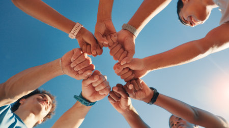 People, team and fist bump in fitness with blue sky below for motivation, unity or mission. Low angle, group or friends with hands together in huddle, circle or solidarity for health and wellnessの写真素材