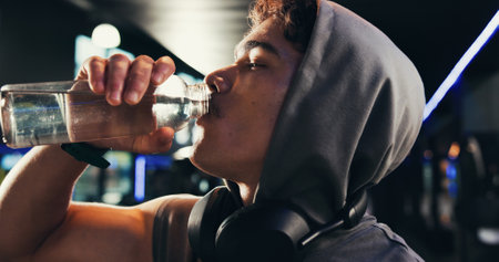 Drinking water, fitness and man in gym, thirsty and minerals with training, tired and workout. Healthy person, liquid or bottle in wellness center, nutrition and fatigue with electrolytes or refreshの写真素材
