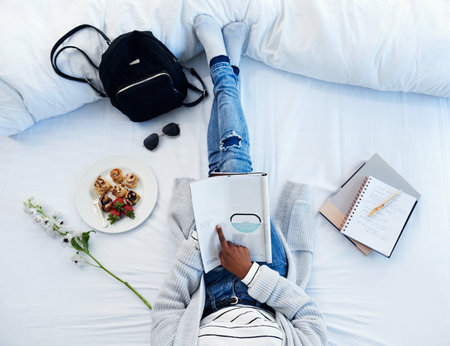 Bed, magazine and above of person reading with food for remote work, content creation and journalism job. Hotel, print and editor with material for travel catalogue, article and portfolio in bedroomの写真素材