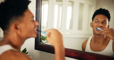 Home, man and dental with toothbrush in mirror, oral care and mouth treatment in morning routine. Reflection, male person and wellness with teeth whitening for gums, hygiene and grooming in bathroomの写真素材