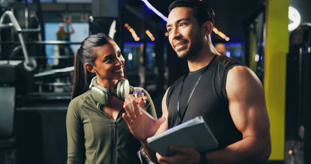 Personal trainer, woman and discussion with tablet at gym for advice, sign up or listen for exercise tips. People, coach and app with membership for training, workout and talking at fitness centerの写真素材
