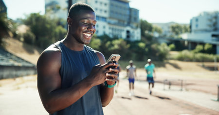 Outdoor, man and chat with smartphone for fitness, online communication and smile on application. Stadium, male person and athlete with mobile for typing message, social media and break for exerciseの写真素材