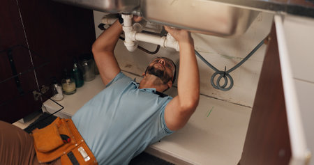 Man, plumber and repair in kitchen, pipe and sink with search for leak, problem solving and fix in home. Person, handyman and check for water, drain and solution on floor for maintenance at apartmentの写真素材