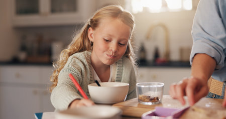 Girl, child and drawing in kitchen at breakfast with parent, help and eating with bonding, care and love. People, kid and food in morning with writing, notes and learning with eduction in family homeの写真素材