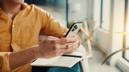 Phone, notebook and hands of man in home for finance journal, planning or investment information. Cellphone, diary and male person with research for online banking on mobile app in apartment.の写真素材