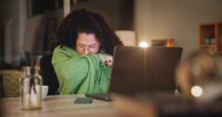 Woman, cough and blanket by laptop in home, sick and study with e learning, video and education. Person, illness and sore throat with pc at night with online course, scholarship and flu in houseの写真素材