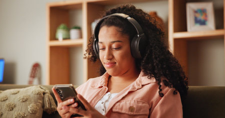 Girl, phone and texting on sofa with headphones, smile and search for funny video in living room. Woman, smartphone and happy with listening to music, streaming and social media on couch at apartmentの写真素材