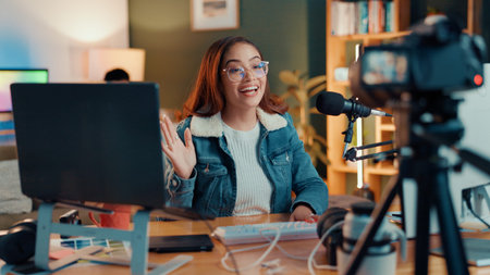 Woman, wave and live stream in home with mic, camera and smilie for chat with audience on social...