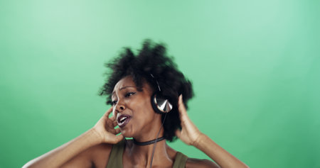 Dance, headphones and singing with black woman in studio for energy, excitement or radio streaming. Music, rhythm and space with happy dancer person on green background for audio subscriptionの写真素材