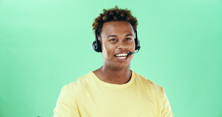 Talking, headset and african man in studio for call center, telemarketing and green background. Lead generation, telesales and happy male agent for sales, inbound marketing and networking by spaceの写真素材