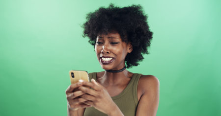 Phone, sad and text message with black woman in studio for communication of bad news or update. App, crying and social media with unhappy African person on green background for mobile notificationの写真素材