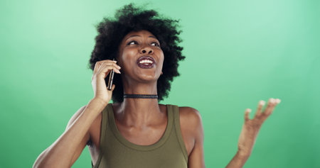 Surprise, phone call and black woman in studio, talking and conversation with contact. African person, space or happy model with cellphone, shocked or discussion with app or smile on green backgroundの写真素材