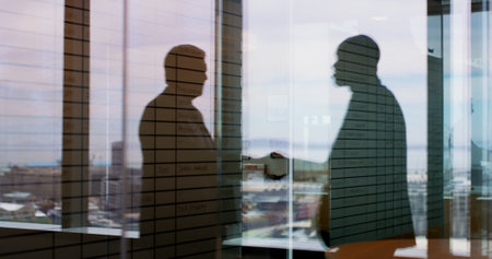 Businessmen, silhouette and window with handshake in double exposure for deal or agreement. Colleagues, employees or shaking hands with vision for negotiation, meeting or partnership in cityの写真素材