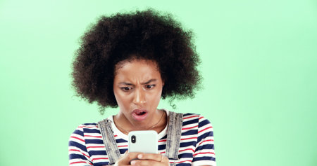 Green background, phone or black woman with surprise for breaking news, mockup and online scam. Space, stress and shocked African girl with mobile app for reading error, notification alert or studioの写真素材