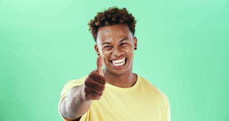 Portrait, thumbs up and black man in studio with yes, thank you and winning hand sign on green background. Winner, smile and model isolated with gesture for support review, success or good job emojiの写真素材