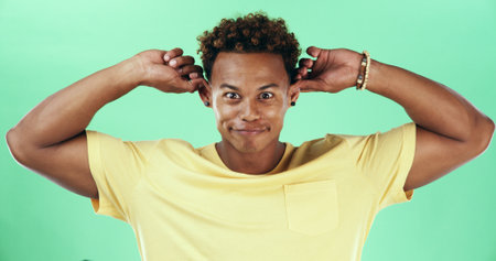 Silly, funny face and smile with black man on green background in studio for humor, joke and meme. Portrait, crazy and comedy with happy African student, model and playful with goofy expressionの写真素材