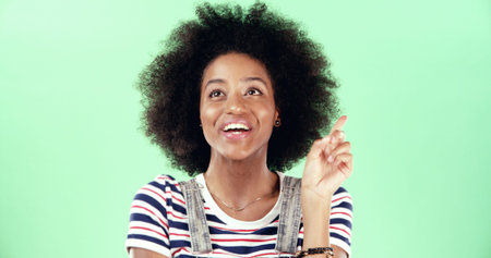 Thinking, black woman and pointing with idea in studio for solution, answer or afro with a smile. Excited, female person and aha moment on green background with space, positive and problem solvingの写真素材