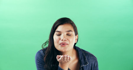 Woman, gesture and blowing kiss in studio for flirting, show attraction and romance icon. Mockup space, female person and smile with love emoji for valentines day, affection sign and green backgroundの写真素材