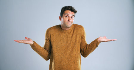 Portrait, shrugging and question with man in studio for doubt, problem solving or solution. Emoji, hand gesture and uncertain with confused person on white background for answer, decision or mistakeの写真素材