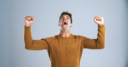 Happy man, fist pump or celebration in studio for winning, victory or bonus on a white background. Excited, male person or model shouting in joy with relief for achievement, promotion or winner prizeの写真素材